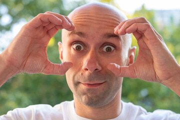 Curious bald man with hands framing eyes, Surprised male gesturing with hands making eye circles...