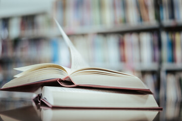 Open book with books piled up on the table in the library. Basic education concept.