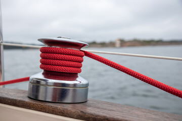 Sailboat winch with red rope of genoa headsail sheet in jammer on yacht deck. Detailed close-up...