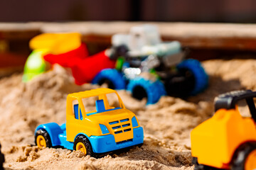 Fototapeta premium Bright toy cars and an excavator standing on the sand. This creates an atmosphere of children's play and creativity.