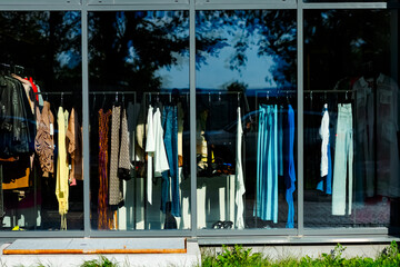 A clothing store window with colorful dresses, jeans and scarves reflecting the trees and sky....