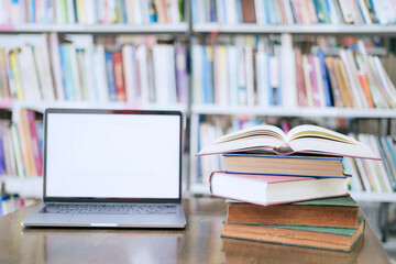 There is a laptop with a white screen and a book placed on the table in the library.
