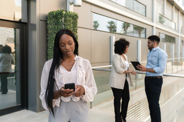 African american Businesswoman using smartphone while colleagues discussing in background outdoors