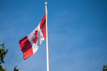 Canadian national flag on a flagpole against a clear blue sky, featuring the iconic red maple leaf symbolising unity, pride, and heritage.