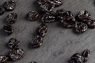 black prunes made from small plums, piled on a board made of black stone dried plum fruits, close up