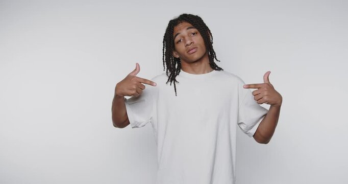 footage of young man playfully gestures towards himself, portraying self-assertion and pride on light background