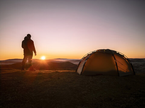 An explorer and his wild camping tent on a hill in England at sunrise