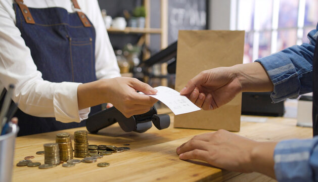 Close-up of hands exchanging receipts and payments at a store counter, showing customer and cashier interaction with coins, receipts, and an EDC machine - Powered by Adobe