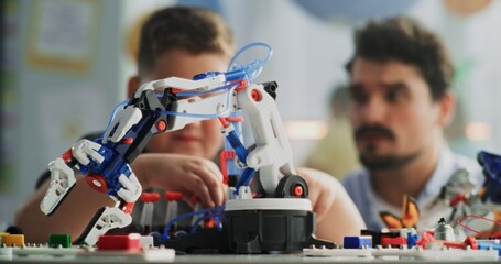 Elementary School Boy Sitting at the Desk, Studying Model of Innovative Robotic Arm. Teacher...