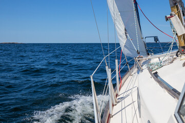Luxury sailing yacht under genoa and mainsail cutting through waves of the Baltic Sea, Gulf of Finland. View from deck to bow, mast, and sails, emphasizing speed, motion, and yachting adventure