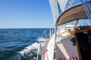 Luxury sailing yacht under genoa and mainsail cutting through waves of the Baltic Sea, Gulf of Finland. View from deck to bow, mast, and sails, emphasizing speed, motion, and yachting adventure
