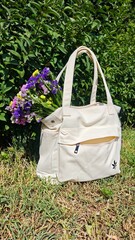 A white canvas tote bag with a bouquet of colorful wildflowers rests on green grass under bright...