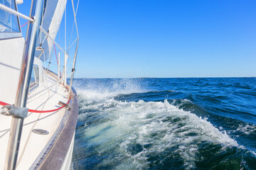 Luxury sailing yacht under genoa and mainsail cutting through waves of the Baltic Sea, Gulf of Finland. View from deck to bow, mast, and sails, emphasizing speed, motion, and yachting adventure