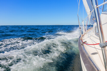 Obraz premium Luxury sailing yacht under genoa and mainsail cutting through waves of the Baltic Sea, Gulf of Finland. View from deck to bow, mast, and sails, emphasizing speed, motion, and yachting adventure