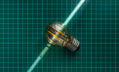 a single clear light bulb with visible LED filaments lies diagonally on a green cutting mat, with a...