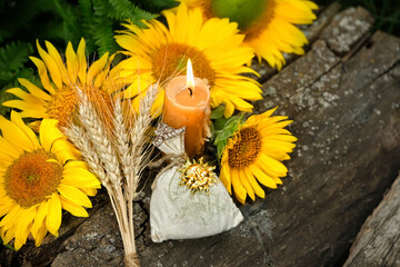 Burning candle, wheat ears, sunflowers and witch bag with symbolic sun amulet in forest, natural background. Witchcraft, magic practice. esoteric spiritual ritual for Lammas, Lughnasadh