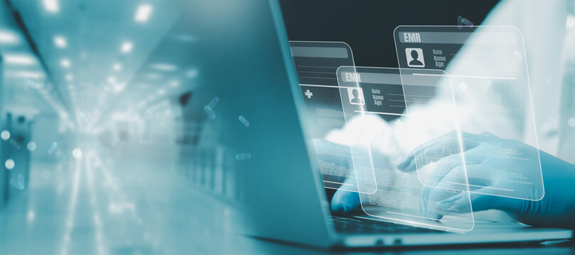 Digital health data management concept featuring doctor wearing blue gloves using laptop to access futuristic EMR interfaces with transparent digital patient records in hospital environment.