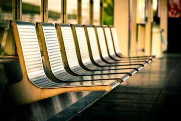 Row of empty metal seats or waiting bench at a train station platform, bathed in warm sunlight