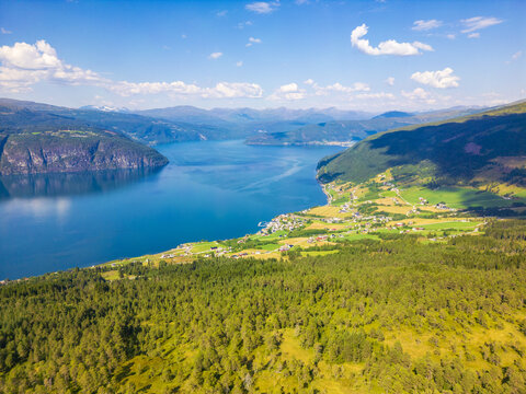 Aerial view of the serene fjord cutting through verdant hillsides, reflecting the azure sky above, a tranquil panorama of nature's grandeur, Utvik, Vestland, Norway.