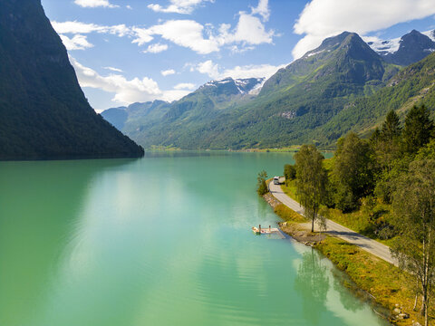 Aerial view of the turquoise lake mirroring the dramatic mountain landscape under a vibrant blue sky, Oldevatnet, Vestland, Norway.