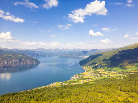 Aerial view of a deep blue fjord snaking between steep, verdant slopes under a vast, bright sky, Utvik, Vestland, Norway.