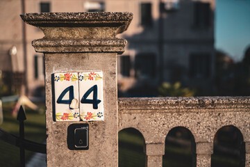 House number 44 displayed on decorated ceramic tile on a stone pillar