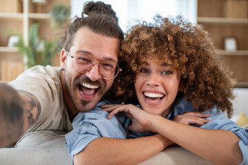 Fototapeta premium Happy couple taking a selfie on the couch, sharing a laugh