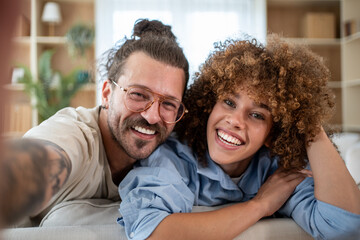 Fototapeta premium Happy couple taking selfie on sofa at home smiling and relaxing