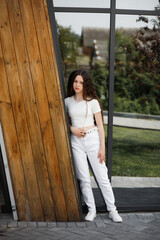 A girl in white trousers and a white blouse near a mirrored wall, leaning against it.