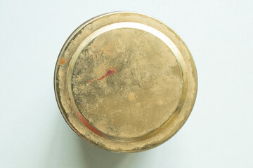 Old metal jar lid with scuffs and rust on the surface, yellow, stands on the table