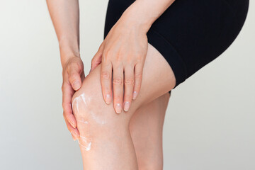 A young woman applying an anesthetic cream to the knee joint area, she is experiencing pain in it after training. Woman applying cream to dry skin in the knee area	
