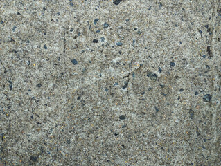 ​A top-down view of an old concrete surface with cracks and small gravel inclusions. The rough, grainy texture and gray tones create a detailed abstract background that can be used for design purposes