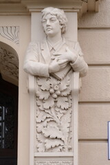 A beautiful Art Nouveau facade sculpture of a young woman. The detailed figure, with long hair cascading over her shoulders, rests on an ornate corbel. 