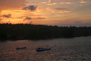 Fishing boats floating on the calm coastal waters during a vivid orange sunset, ideal for tourism...