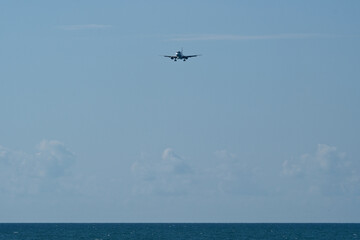 Airplane flying in the blue sky over the sea with white clouds. Airplane in the blue sky with white...
