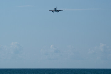 Airplane flying in the blue sky over the sea with white clouds. Airplane in the blue sky with white clouds above the sea.
