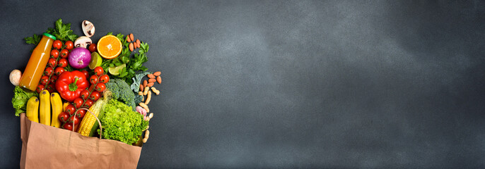 Paper bag full of different healthy food on dark background. Wide banner. Free space for text or...