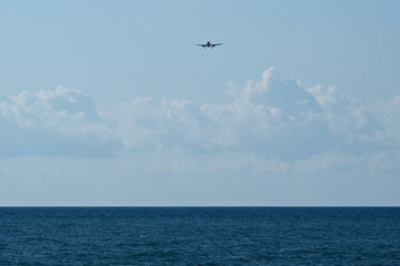 Airplane flying in the blue sky over the sea with white clouds. Airplane in the blue sky with white clouds above the sea.