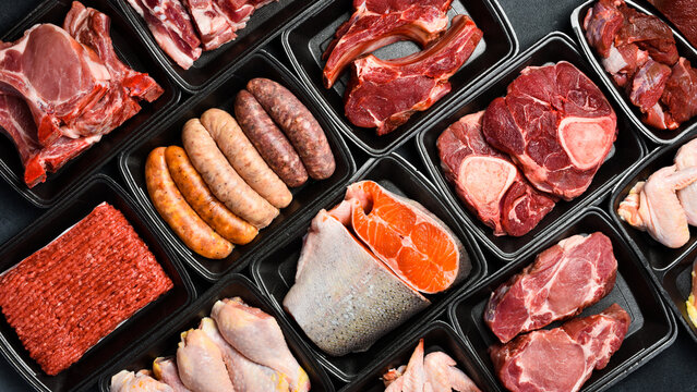Black plastic packaging trays from supermarket with different types of fresh raw meat cuts, fresh beefbeef steaks, fish and variety meats in boxes from above - Powered by Adobe