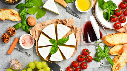 Cheese and wine background. Brie cheese, glasses of wine, nuts and grapes on a table with basil,...