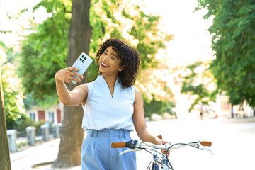 Young woman taking selfie while walking with bicycle in park