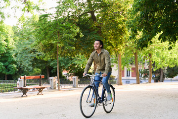 Young man riding bicycle in green park enjoying summer day