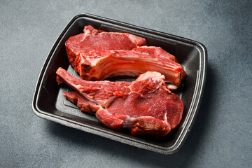 Raw meat. Beef steak on the bone. Meat in a plastic black container from the market. Close-up.
