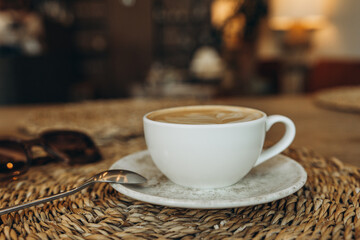 White coffee cup with latte art and sunglasses on a woven placemat
