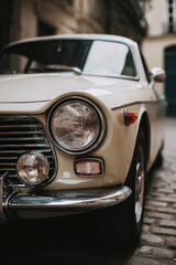 Vintage cream car, classic design. Headlight detail showcases timeless automotive style in urban setting.
