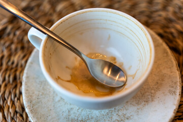 Empty cup with a spoon after enjoying a beverage on a woven placemat
