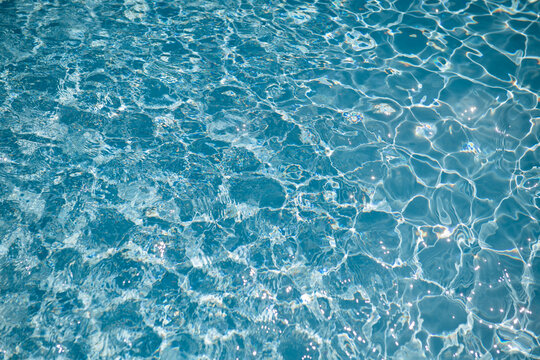 water surface texture of swimming pool with blue tiles background with light ripples from sunshine 