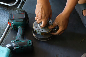 Detailed close-up of a mechanic’s hand performing maintenance on a scooter motorcycle’s CVT (Continuously Variable Transmission) system in a professional workshop. Ideal for illustrating concepts.