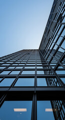 Obraz premium Skyward Gaze: A low-angle perspective of a sleek, modern skyscraper against a clear, cerulean sky, emphasizing its height, geometric design, and architectural details.