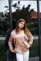 A girl with blond hair in white trousers and a blouse stands by a mirrored wall, leaning against it.